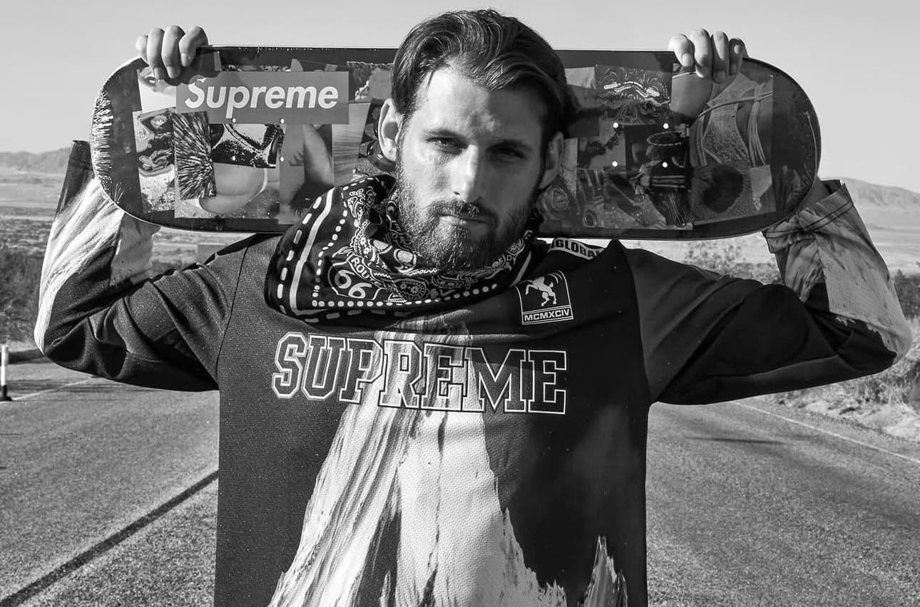 Devin Teer (@devinteerfilms) holding a skateboard behind his head on a desert road